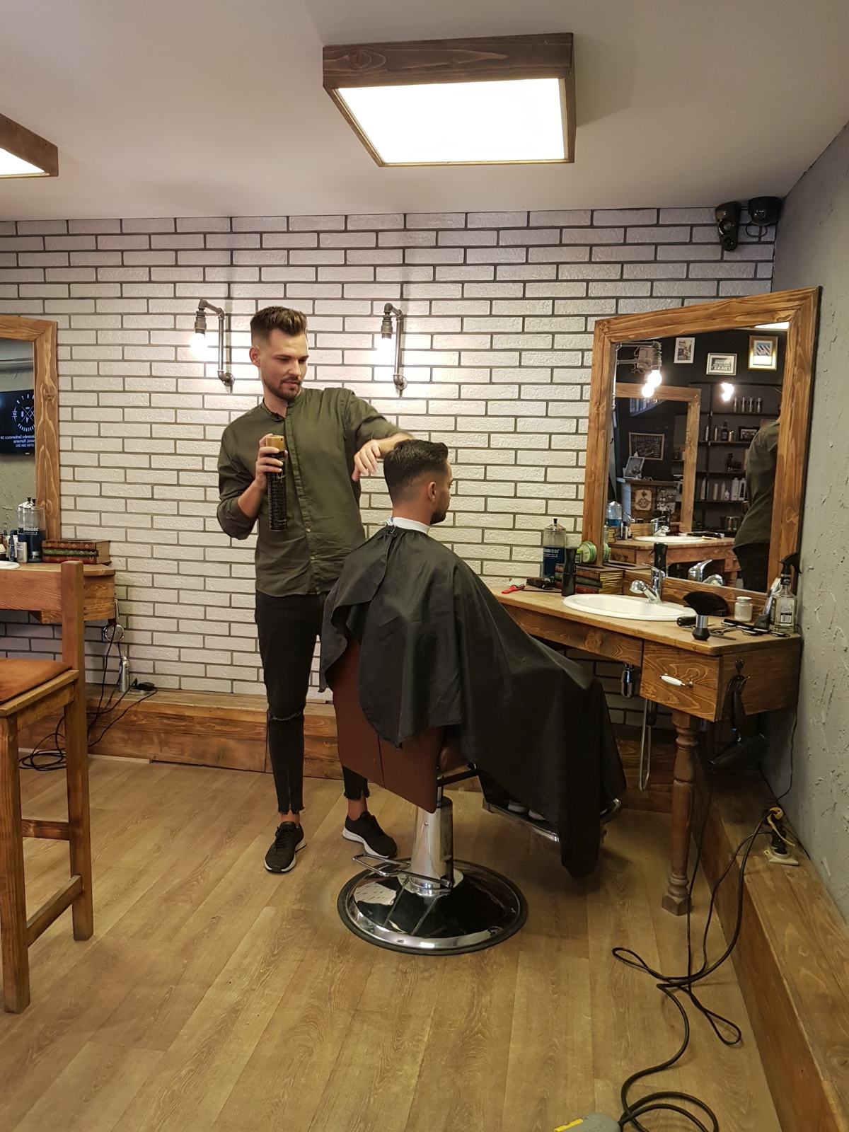 Frizer North Barbershop tunzând un client lângă peretele de cărămidă albă